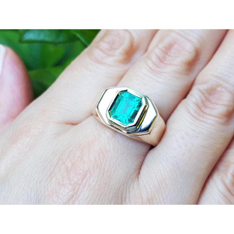 A 14k yellow gold ring for men with a bezel set square natural colombian emerald worn on a hand.