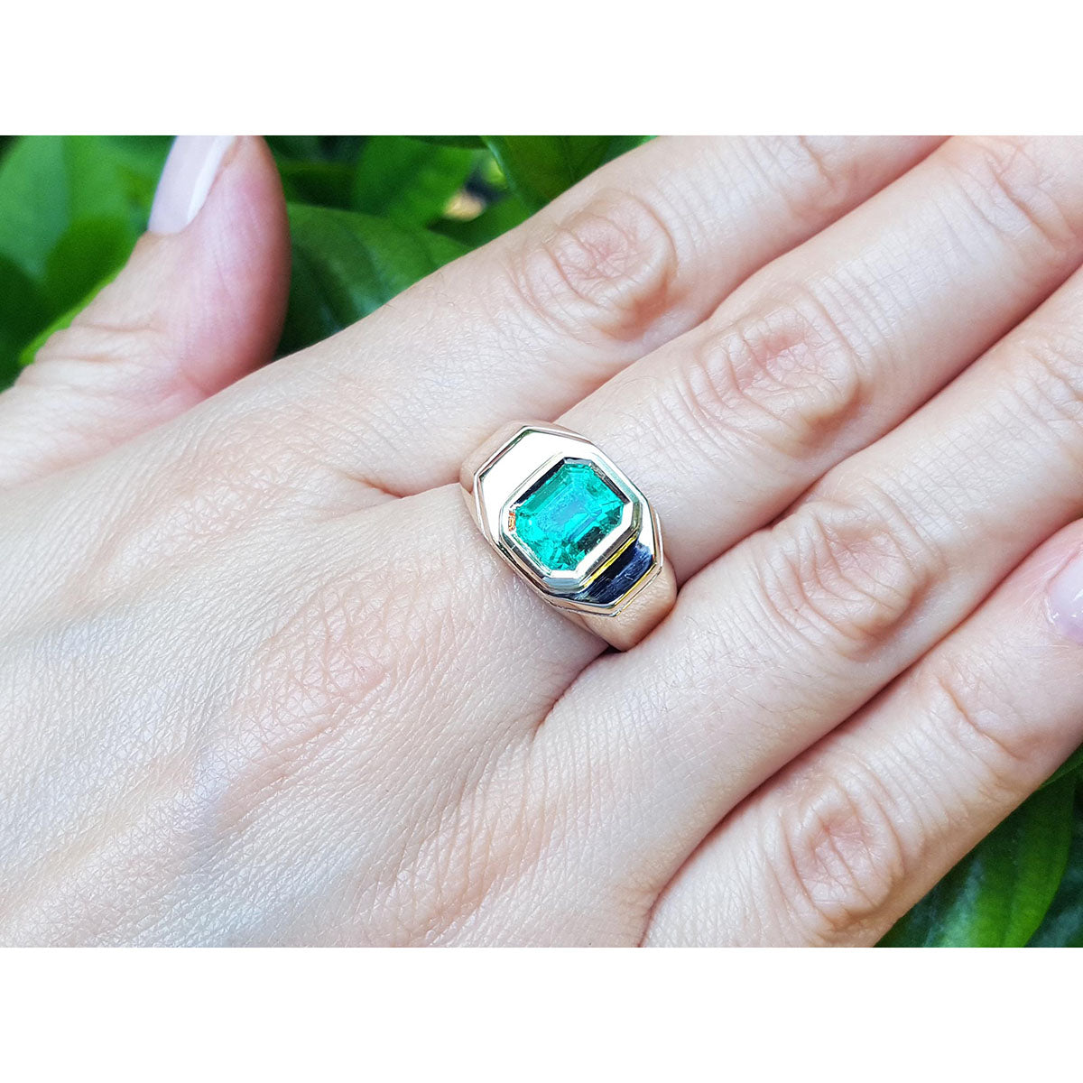A men&#39;s yellow gold ring with a bezel set natural colombian emerald on a hand against a natural background.