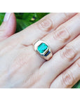 A men's yellow gold ring with a bezel set natural colombian emerald on a hand against a natural background.