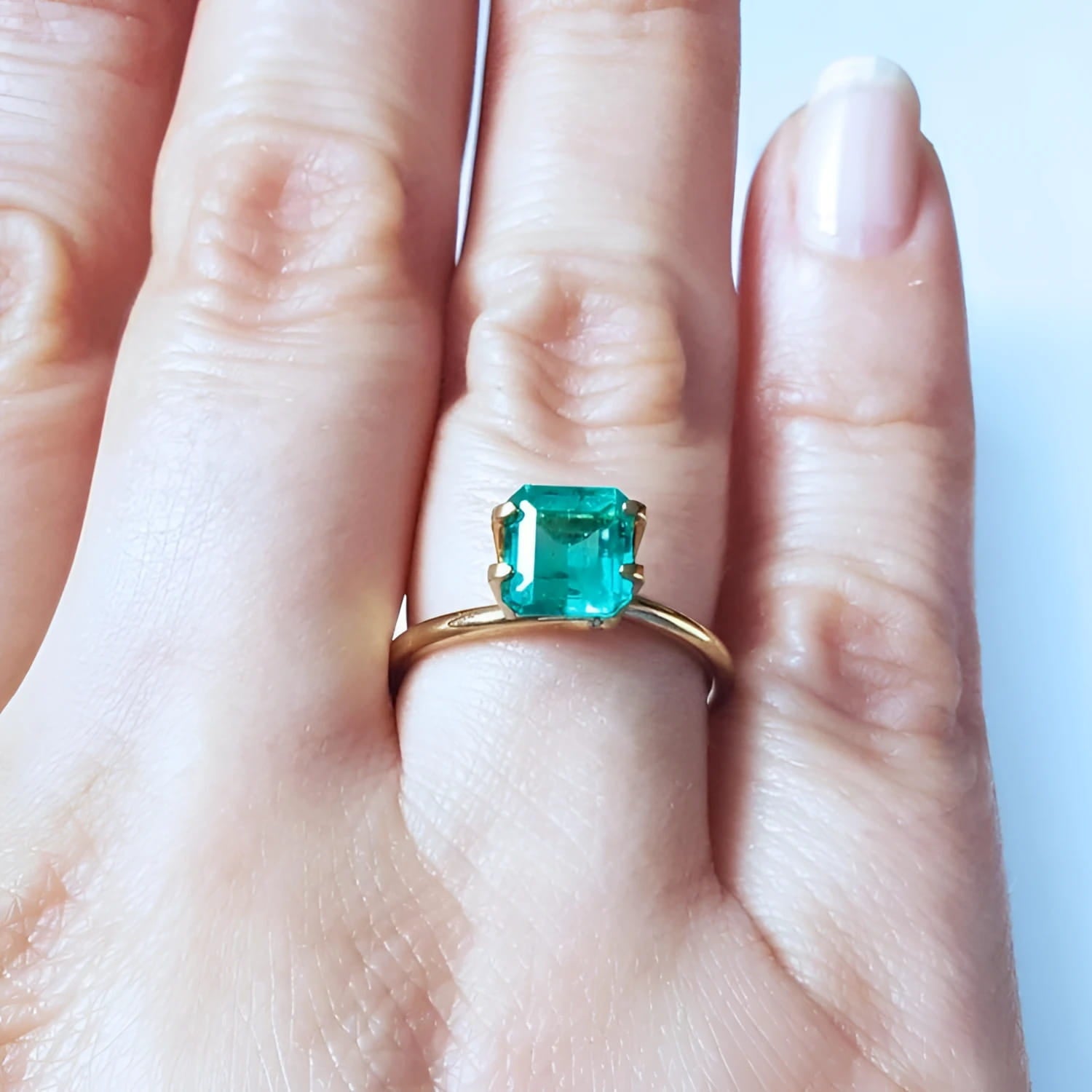 Emerald-cut Muzo Colombian emerald ring with a medium deep bluish-green stone on a gold band.
