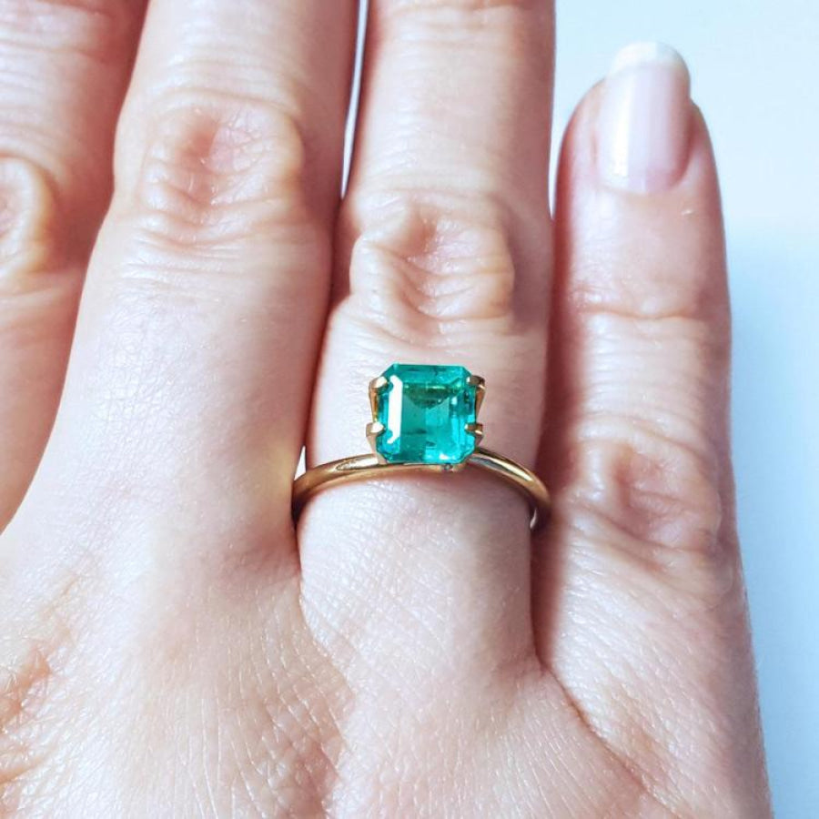 Emerald-cut Muzo Colombian emerald ring with a medium deep bluish-green stone on a gold band.