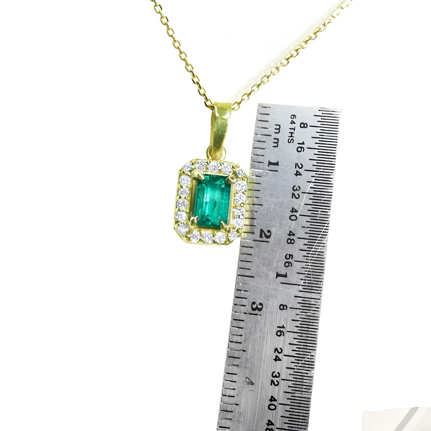 0.75 ct. GIA certified F1 Colombian emerald pendant in 18k yellow gold with diamond halo, next to a ruler.