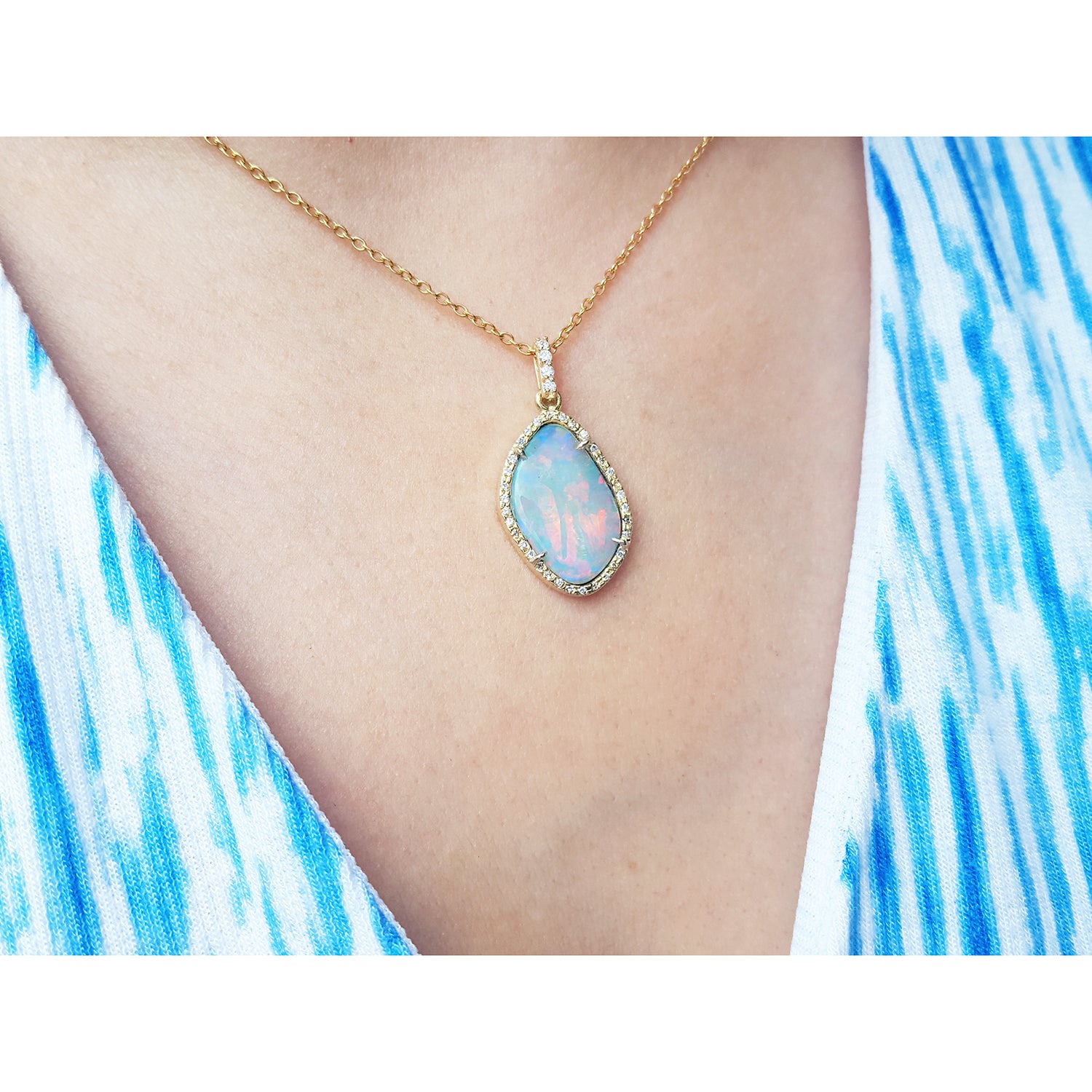 Opal necklace with gold chain on a person wearing a blue and white patterned dress.