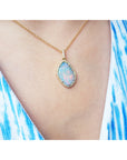 Opal necklace with gold chain on a person wearing a blue and white patterned dress.