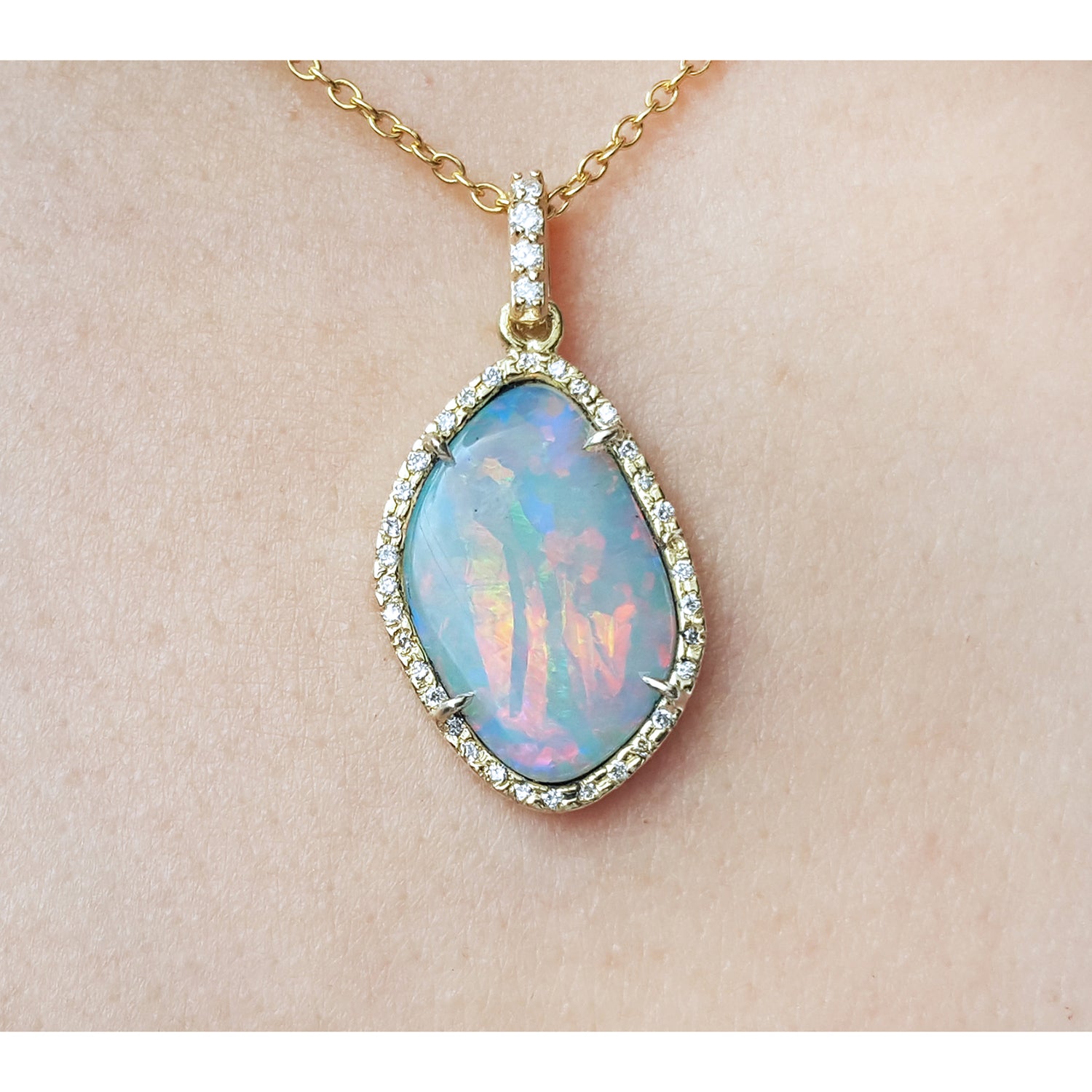 Opal pendant necklace on a gold chain against a beige skin background.