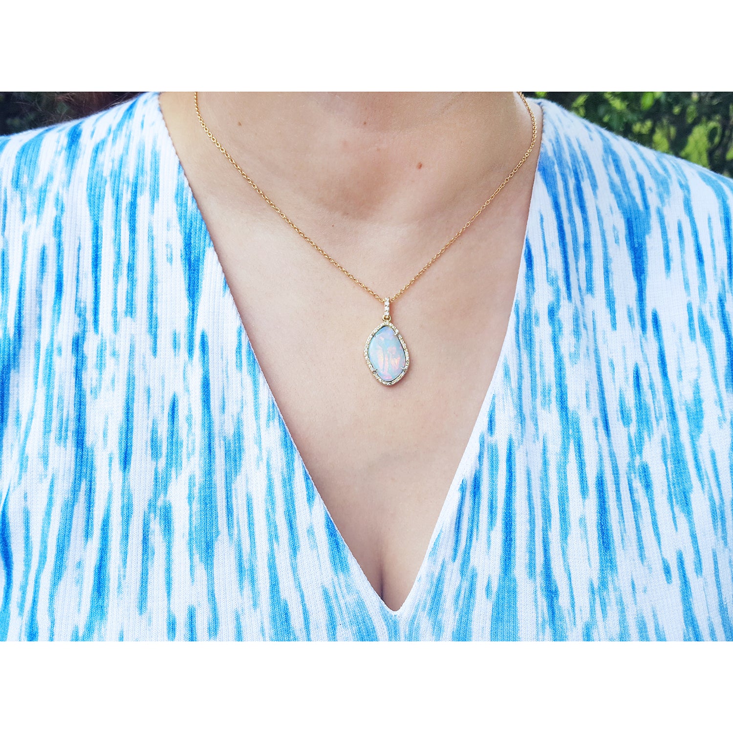 Necklace with a natural opal pendant worn by a woman in a blue and white patterned top.