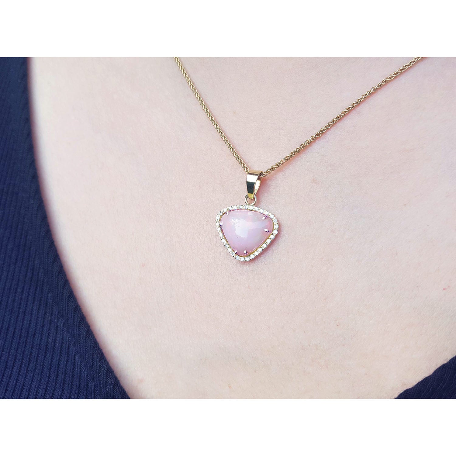 Pink heart-shaped opal pendant on a gold chain worn by a person.