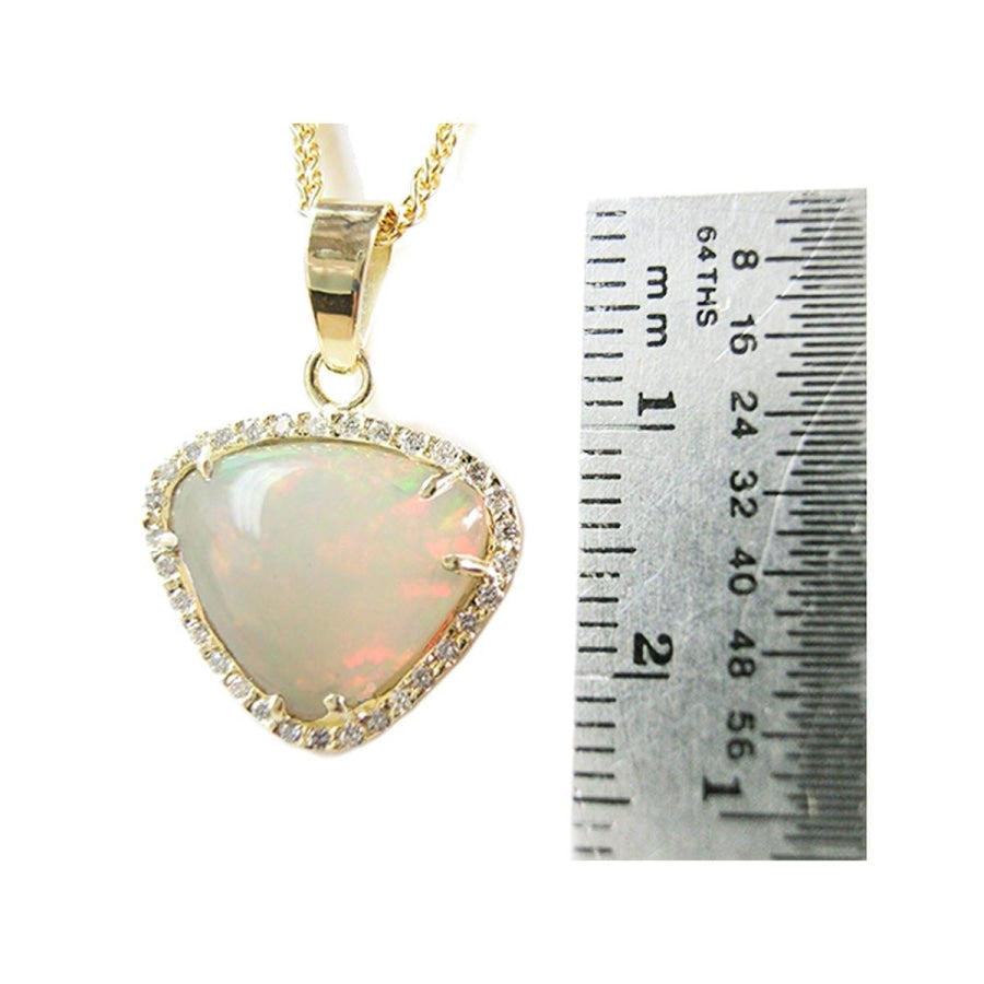 Triangular Australian white opal pendant with red fire, diamond halo, and 14K yellow gold chain, next to a ruler.