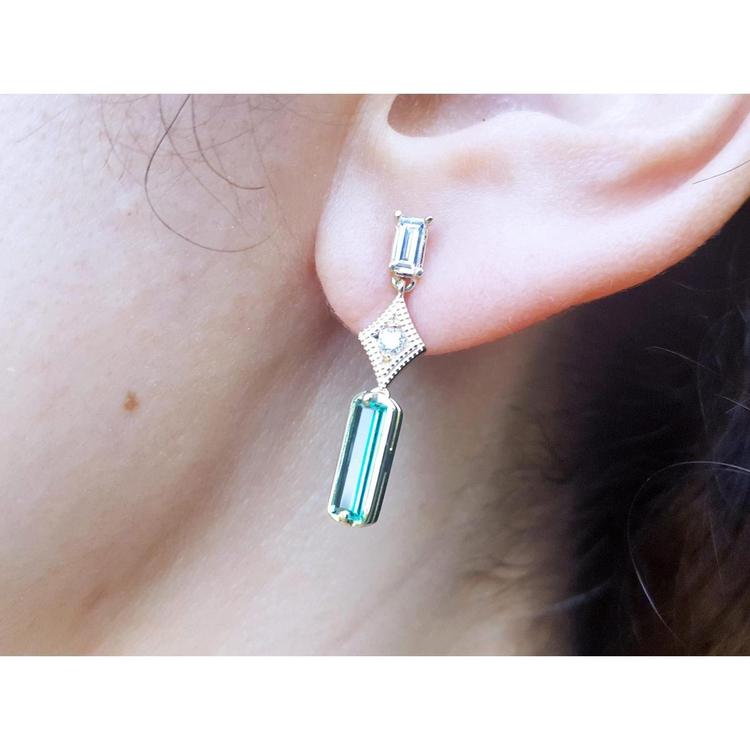 A person wearing a baguette cut colombian emerald and diamond earring.