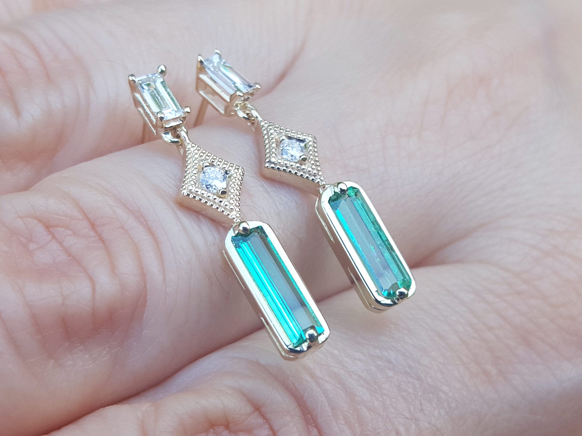 Yellow gold emerald earrings held between fingers