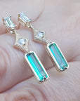 Yellow gold emerald earrings held between fingers