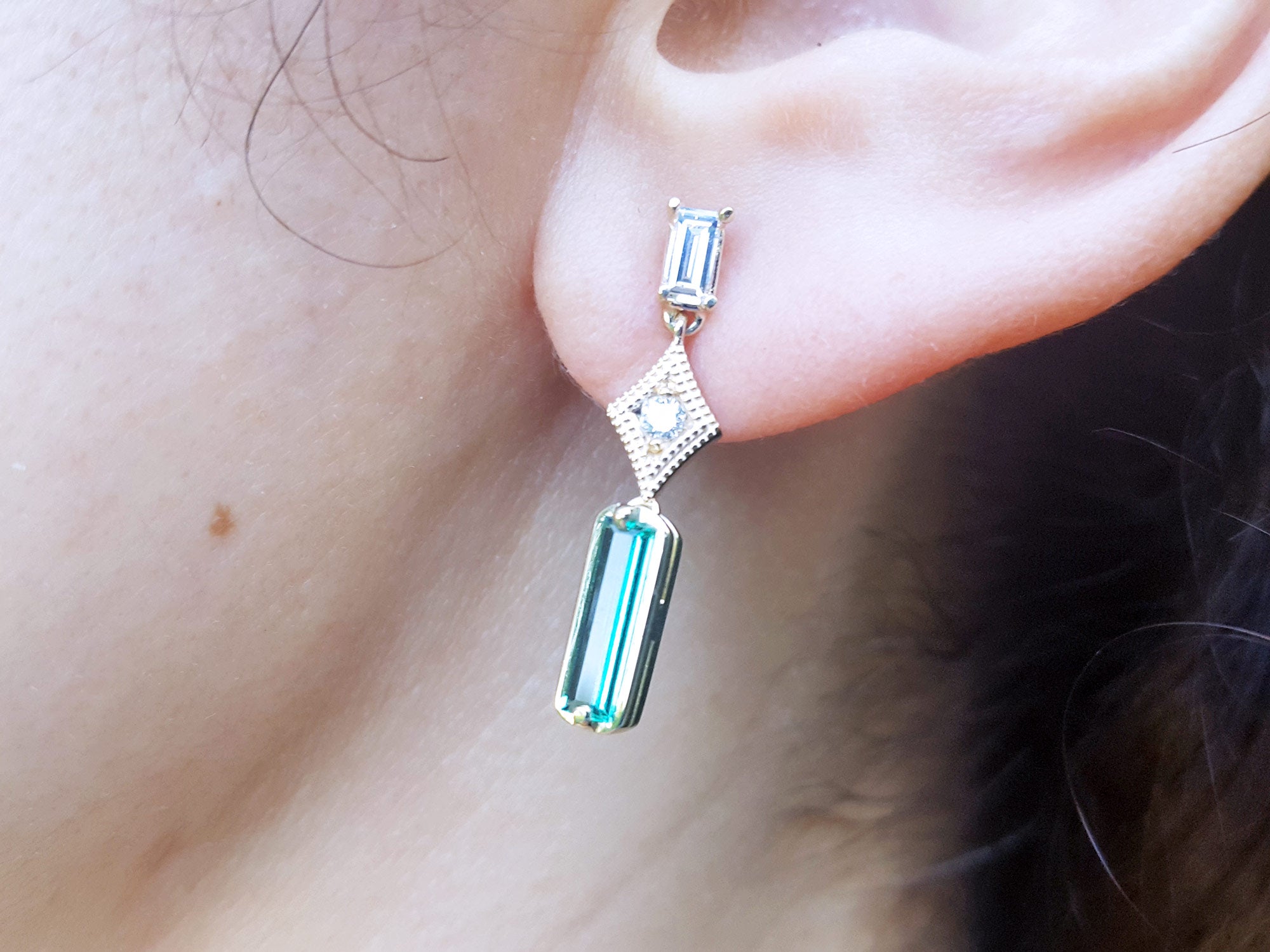 Close-up of a person wearing a baguette cut emerald earring.
