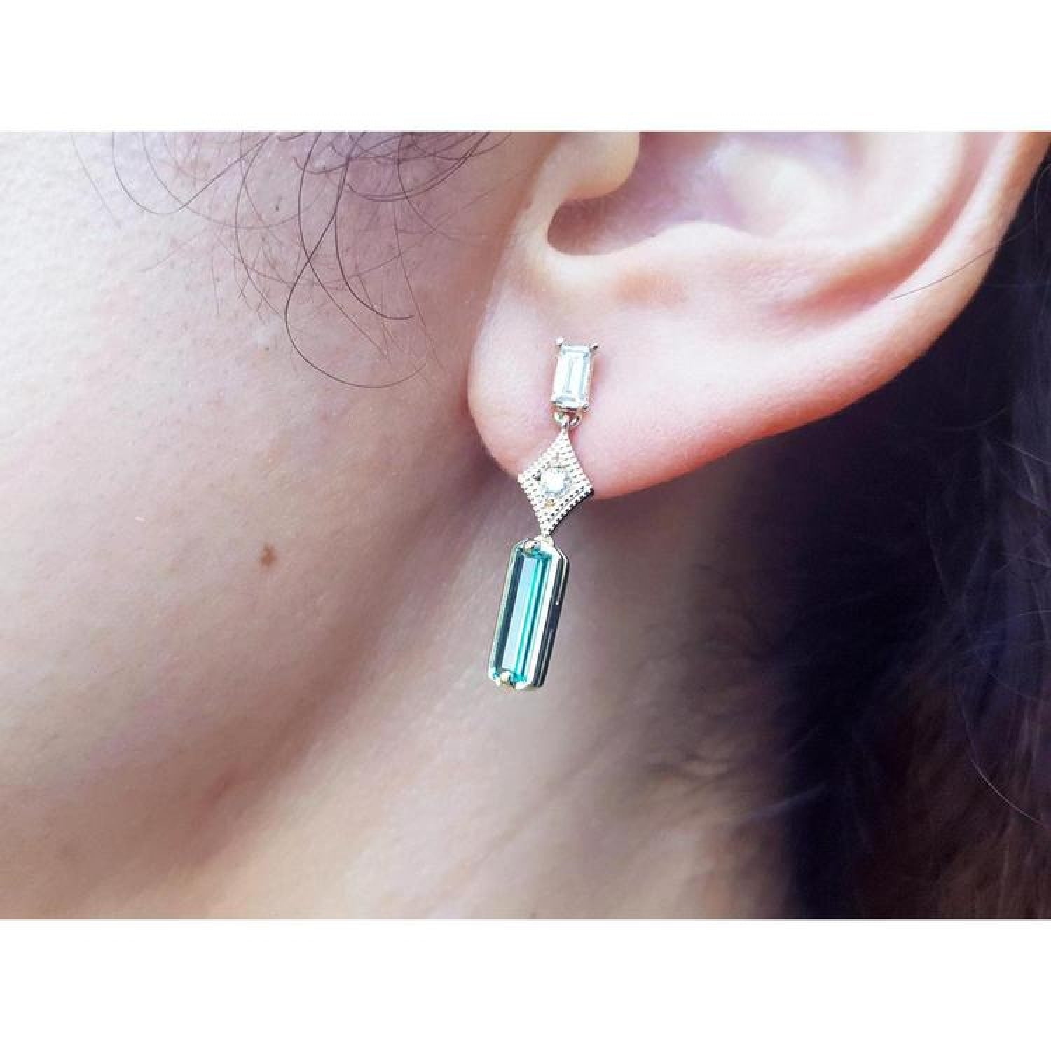 1.05 carat natural baguette cut emerald drop earrings in 14K gold, worn on an ear.