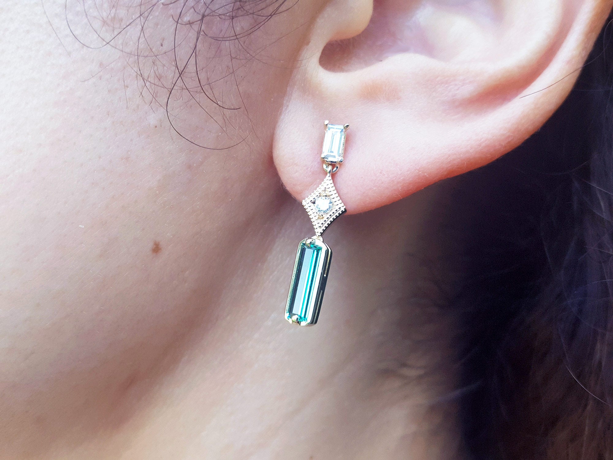 Close-up of an ear wearing an emerald earring with a diamond accent.