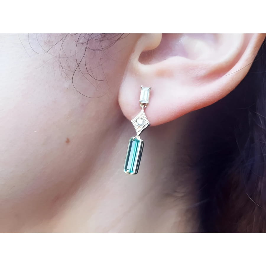 1.05 carat natural baguette cut emerald drop earrings in 14K gold, worn on an ear.