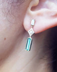Close-up of an ear wearing an emerald earring with a diamond accent.