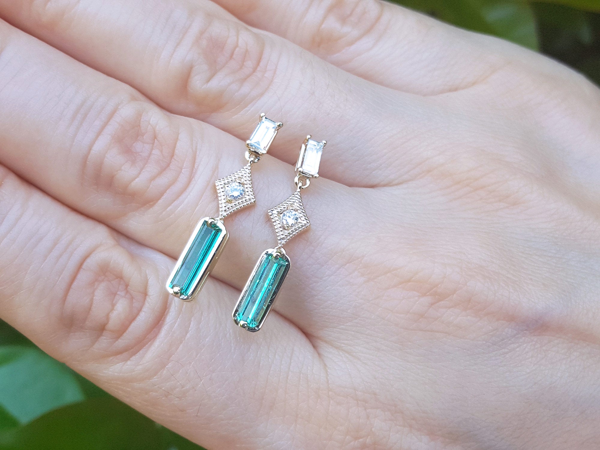 Emerald earrings with diamond stones on a hand against a blurred green background