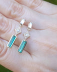Emerald earrings with diamond stones on a hand against a blurred green background