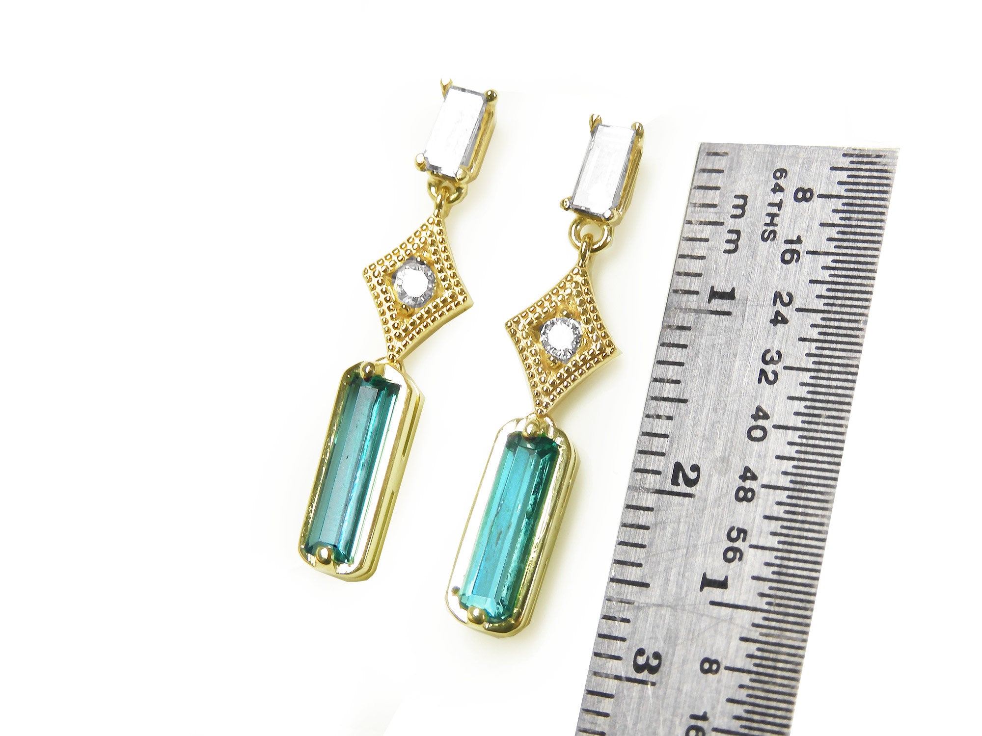 14k yellow gold earrings with Colombian emeralds and diamonds next to a ruler for size reference on a white background