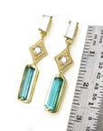 14k yellow gold earrings with Colombian emeralds and diamonds next to a ruler for size reference on a white background