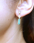 Close-up of an ear wearing a gold emerald and diamond earring with a blurred green background