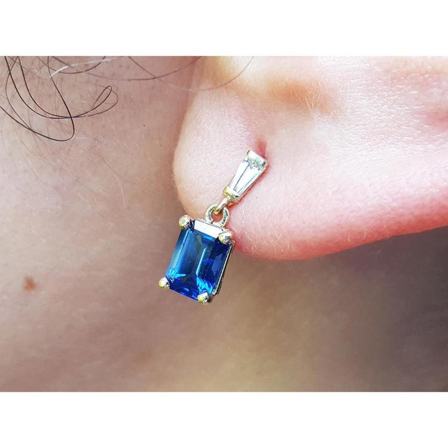 14K yellow gold earrings with emerald cut blue sapphires dangling from baguette diamonds.