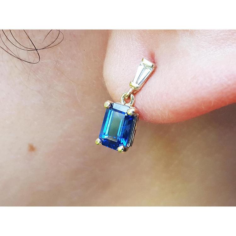 Gold earring with a blue natural sapphire and tapered baguette diamond worn on an ear