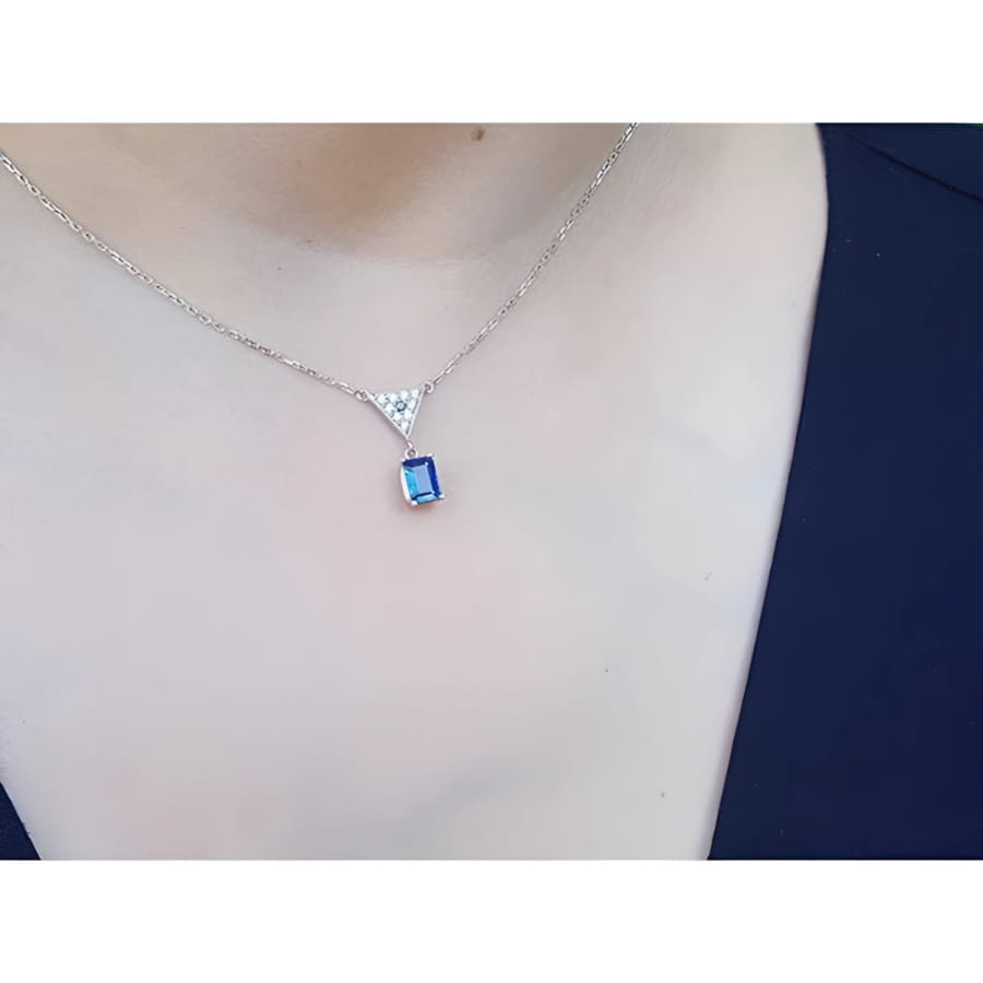 14K white gold necklace with a dangling emerald-cut blue sapphire and pave diamond trillion pendant.