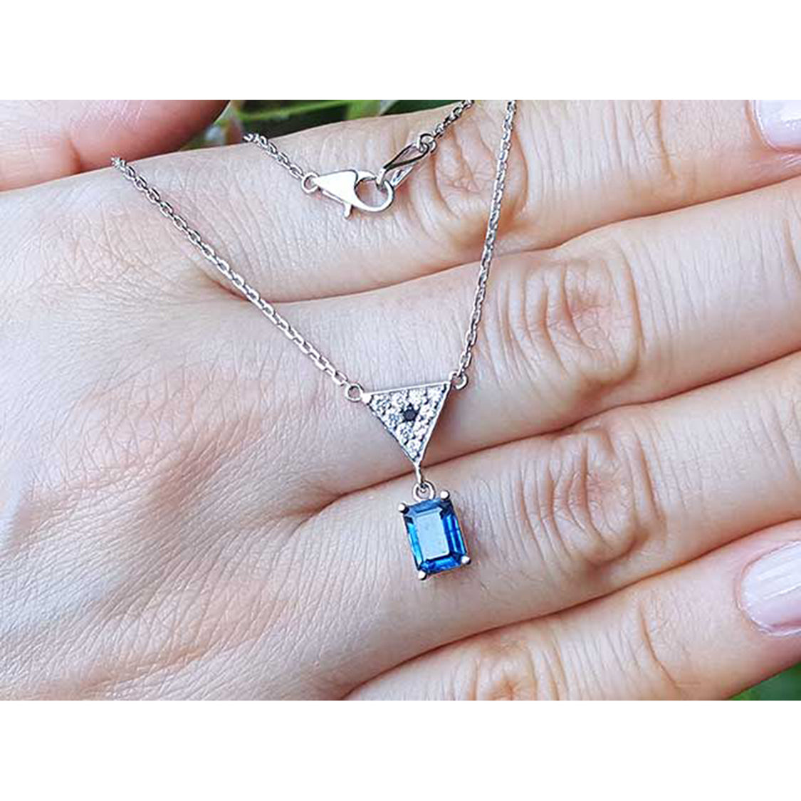 On a hand displaying a natural blue sapphire necklace 14k white gold chain dangling pendant