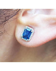 Natural blue sapphire stud earrings emerald cut halo diamond 14k white gold, on a person's ear 