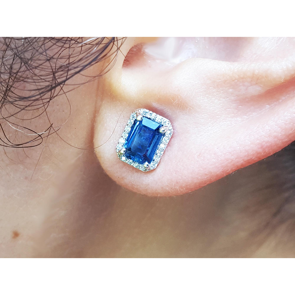 Natural blue sapphire stud earrings emerald cut halo diamond 14k white gold, on a person's ear 