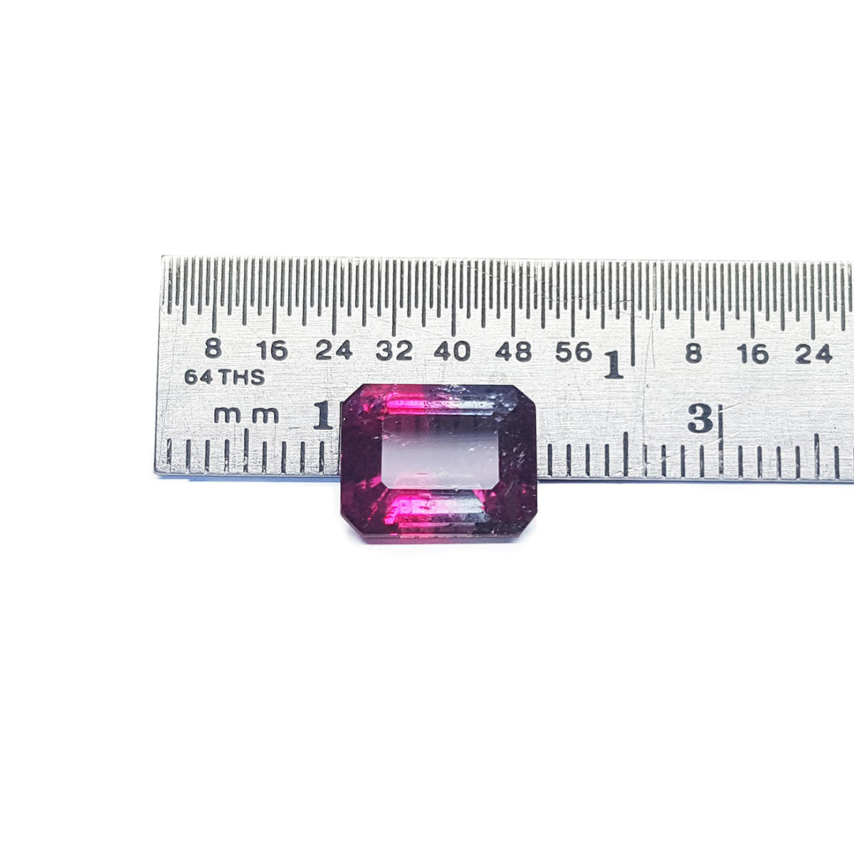 Rectangular pink tourmaline with a ruler for scale on a white background.