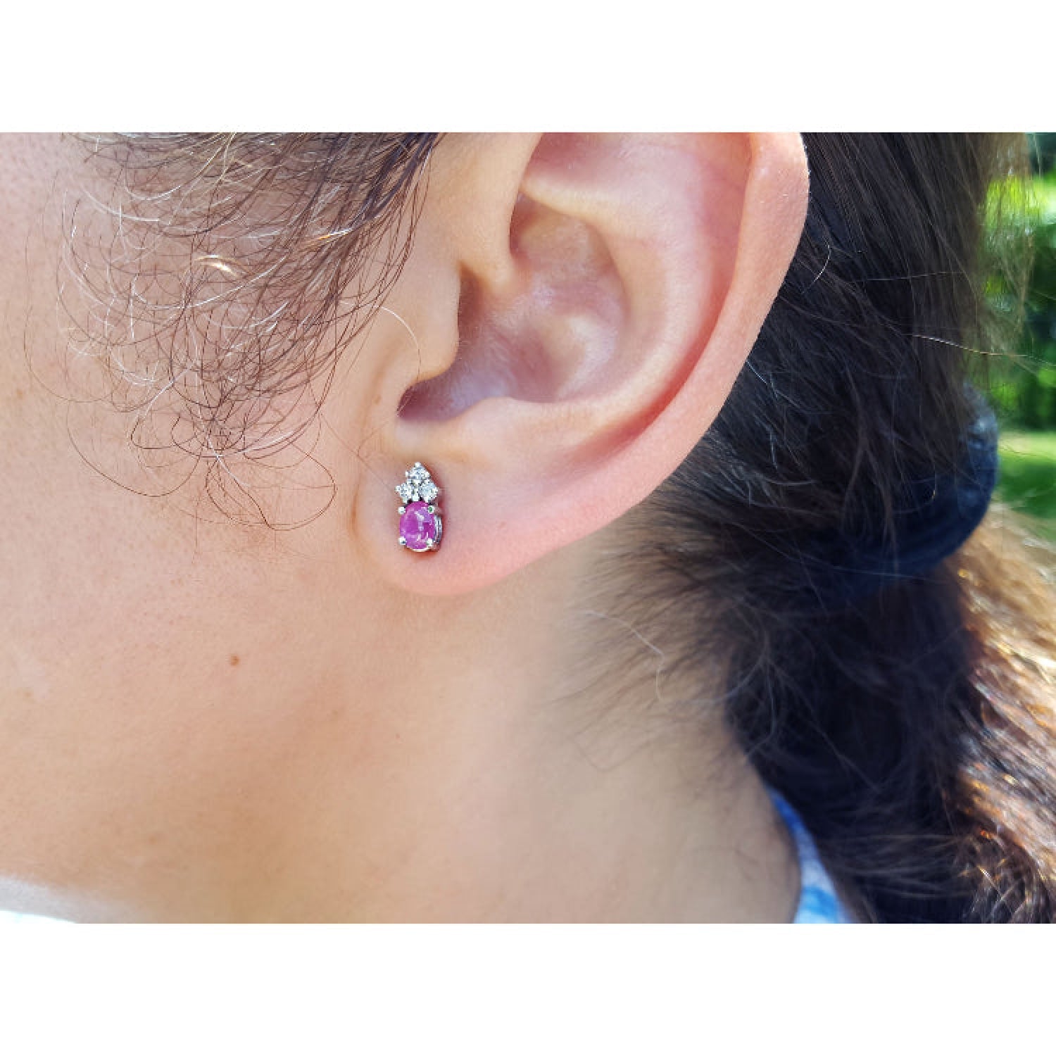 A woman wearing a cabochon pink sapphire earring with a blurred background.