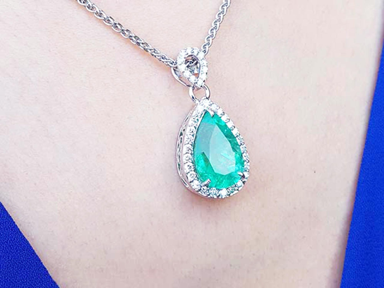 Teardrop-shaped emerald necklace on a person&#39;s neck with a blue background.