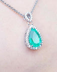 Teardrop-shaped emerald necklace on a person's neck with a blue background.