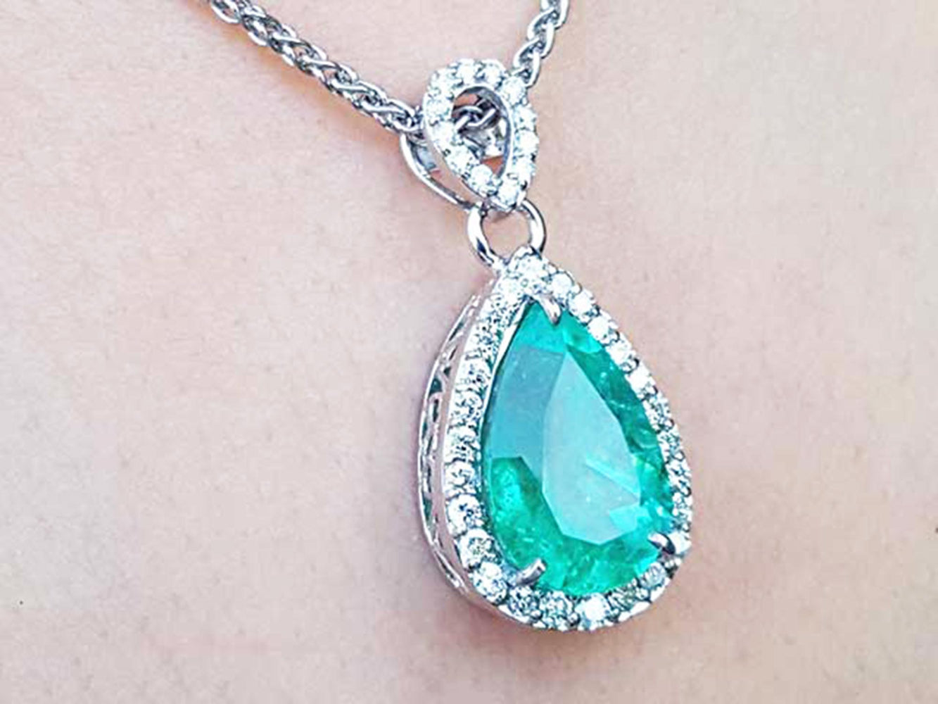 Teardrop-shaped emerald pendant on a chain against a light skin background.