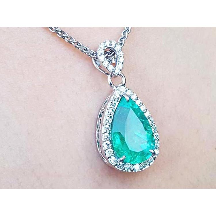 Teardrop-shaped emerald pendant on a chain against a light skin background.