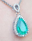 Teardrop-shaped emerald pendant on a chain against a light skin background.