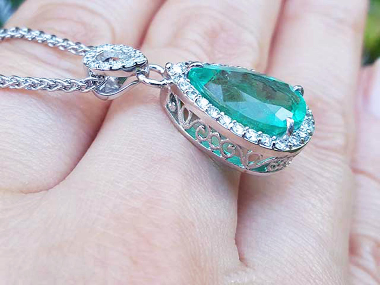 Emerald green gemstone pendant on a gold chain held between fingers.