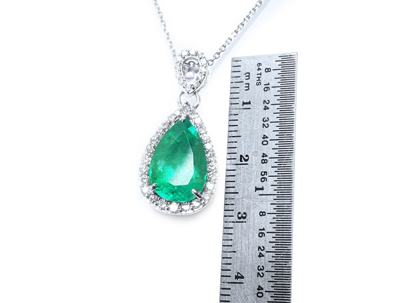 Emerald green teardrop pendant with white gold chain on a white background, accompanied by a ruler for scale.