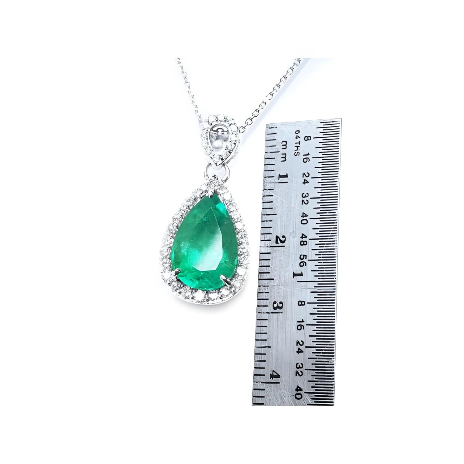 Pear-cut Colombian emerald pendant with diamond halo in 18K white gold, next to a ruler.