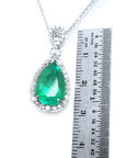 Emerald green teardrop pendant with white gold chain on a white background, accompanied by a ruler for scale.