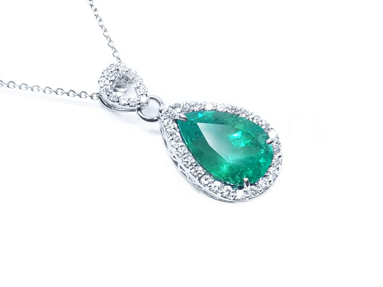 Teardrop-shaped emerald pendant with a halo diamond on a right position and topside view.