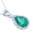 Teardrop-shaped emerald pendant with a halo diamond on a right position and topside view.