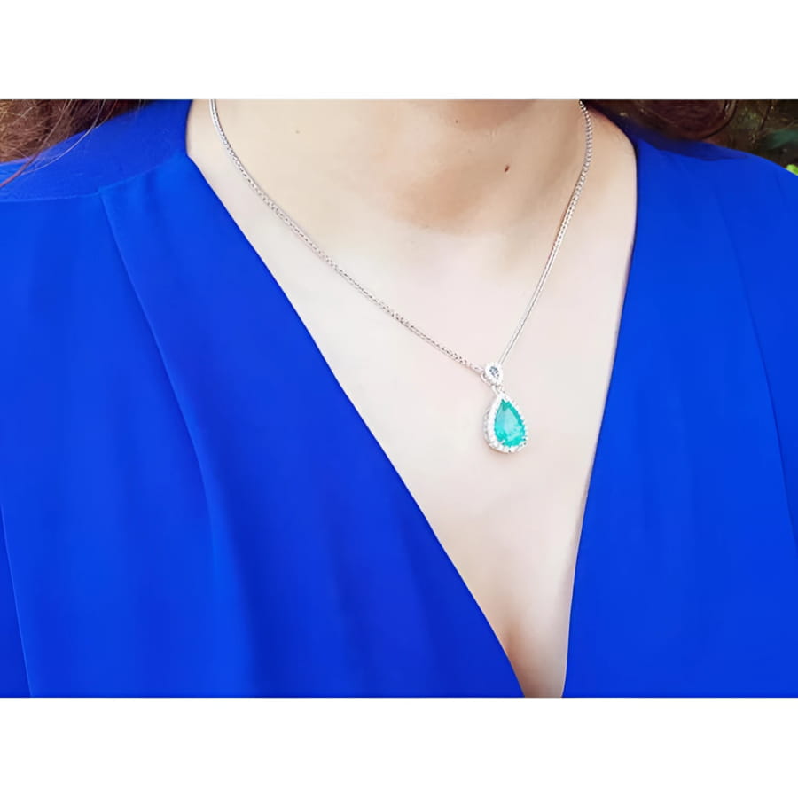 Pear-cut Colombian emerald pendant with diamond halo on an 18K white gold chain, worn on a blue top.