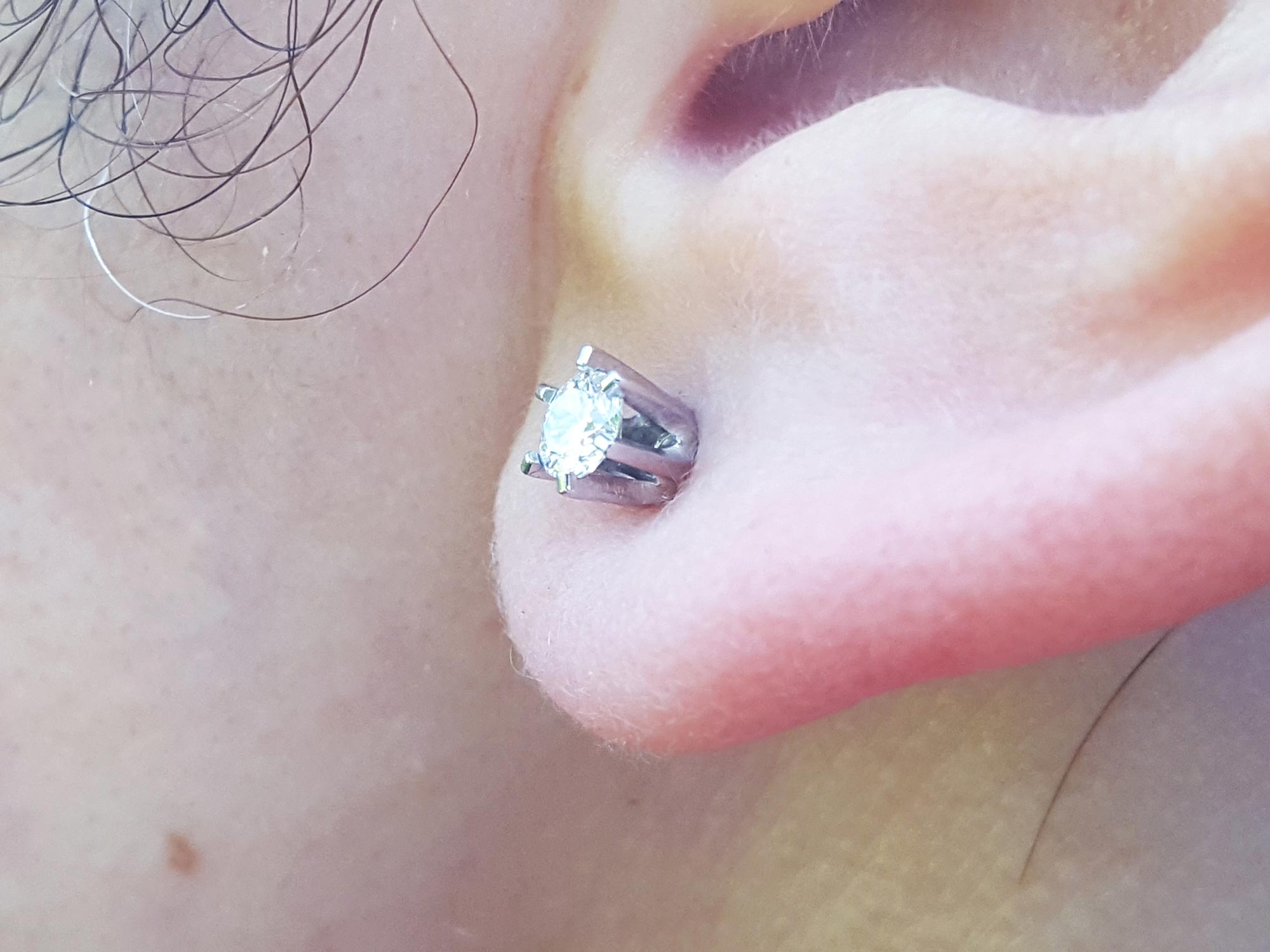 Close up of a 14k white gold diamond stud earring screw back on earlobe.