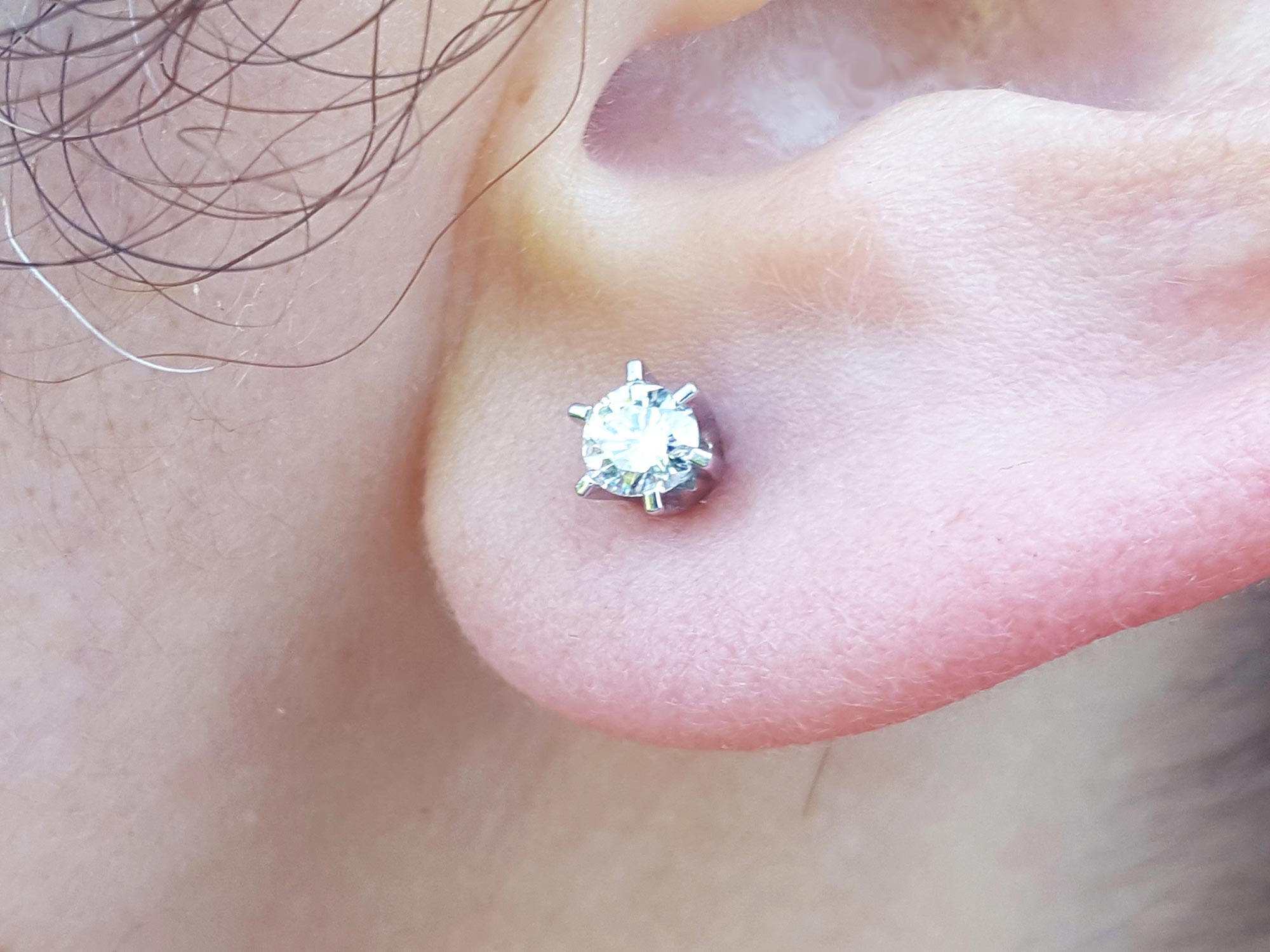 A woman's earlobe wearing a natural diamond stud earring in white gold.