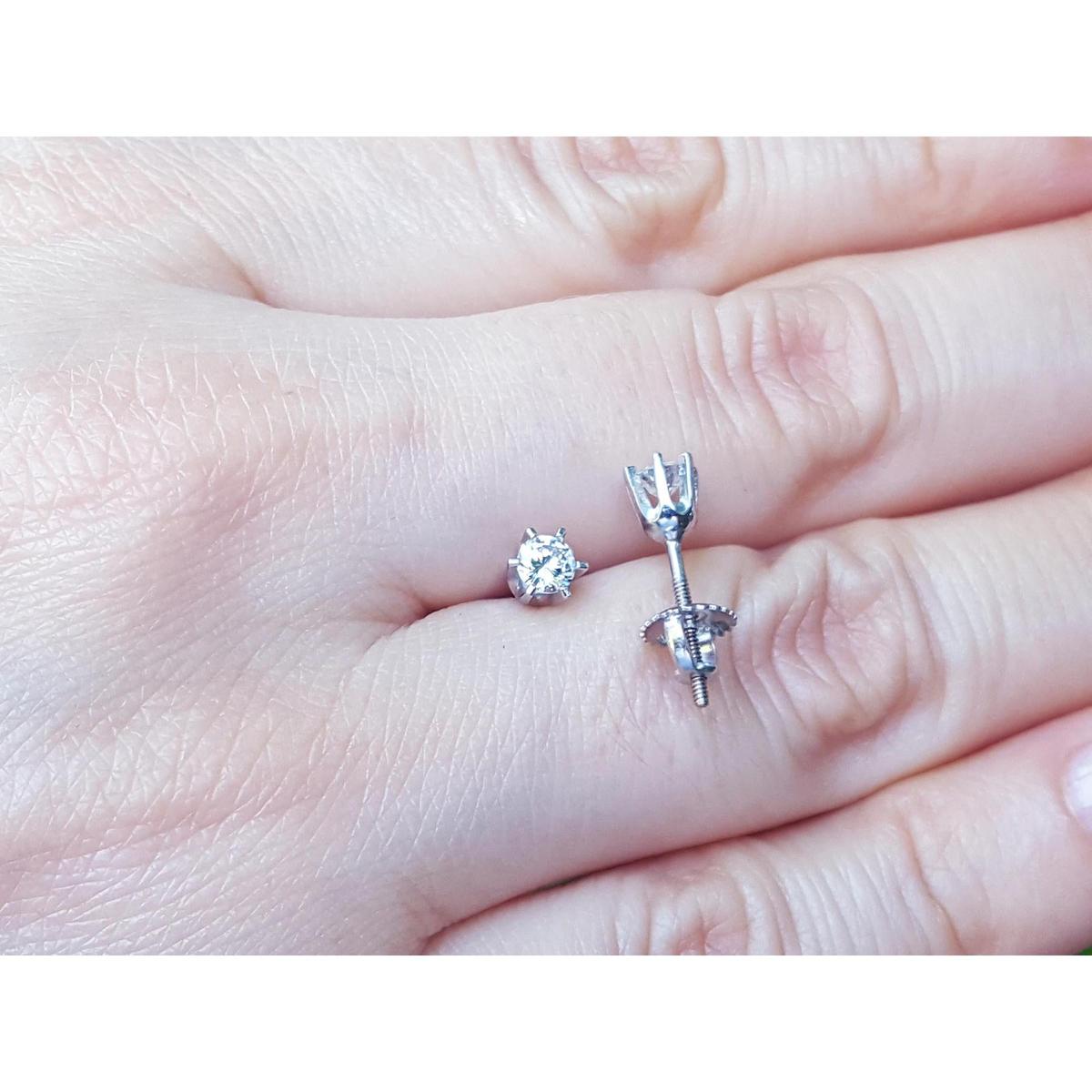 Over a hand displaying a pair of 14k white gold diamond stud earrings screw backs.