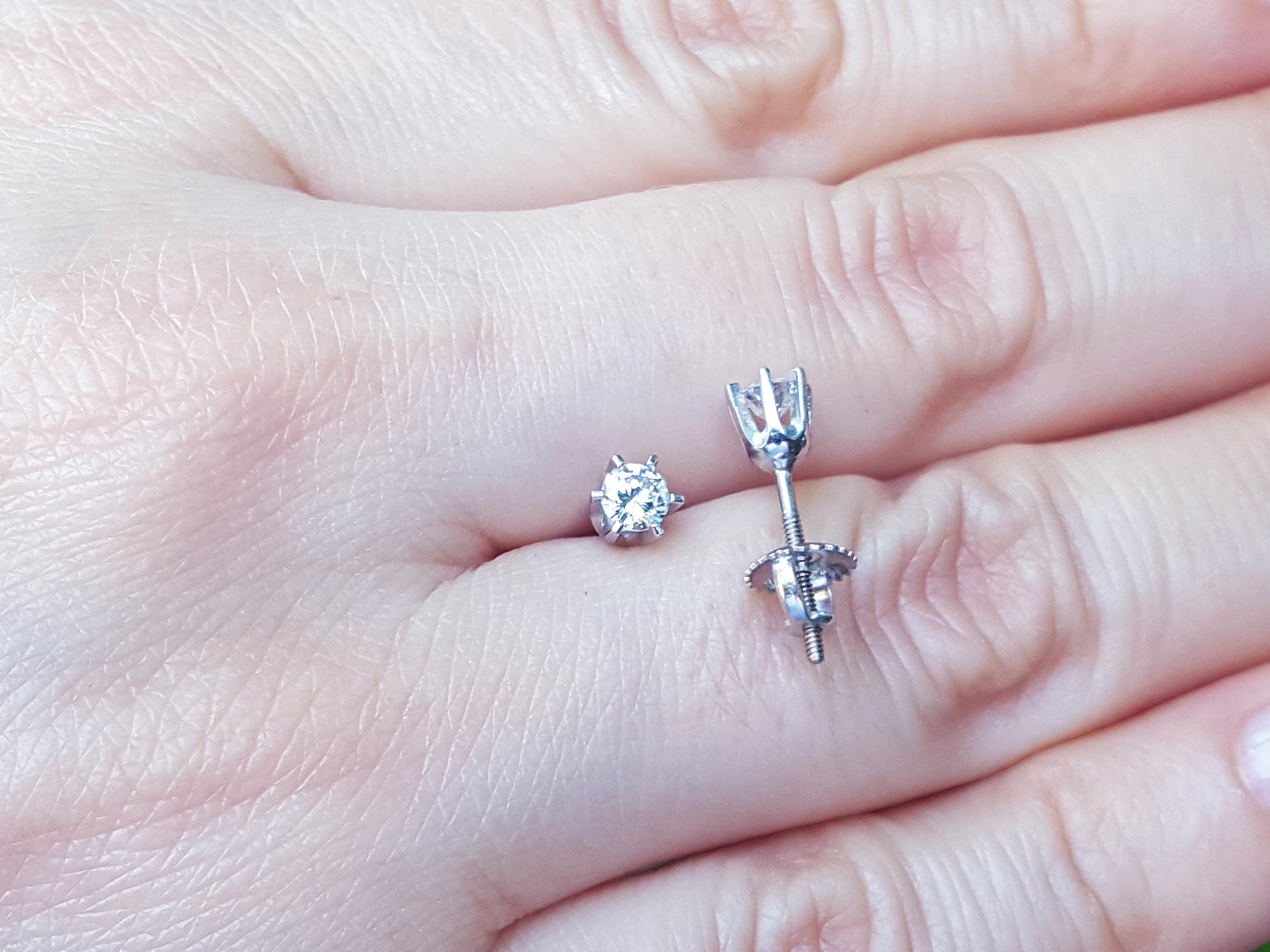 Over a hand displaying a pair of 14k white gold diamond stud earrings screw backs.