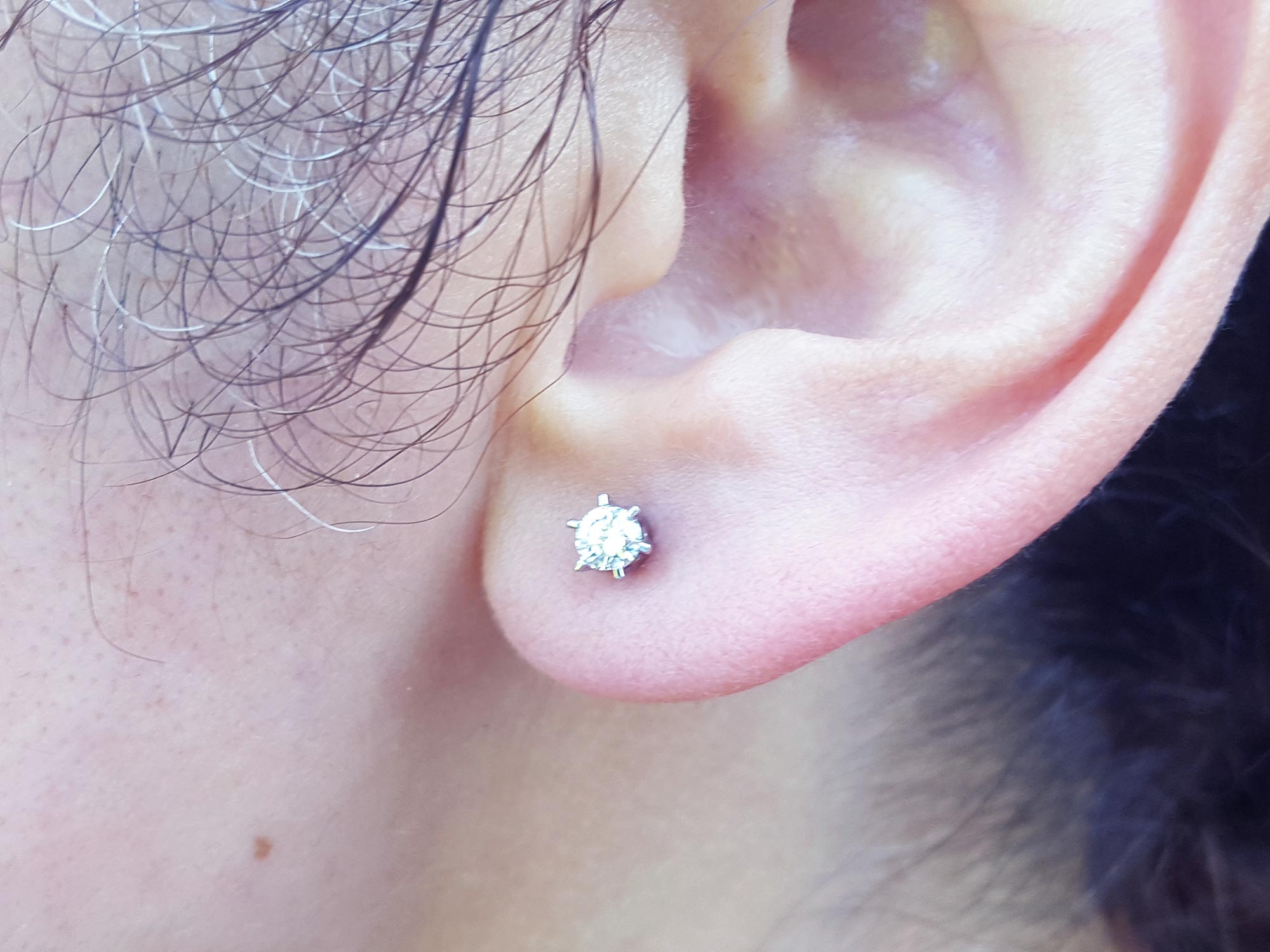 A woman&#39;s ear wearing a 14k white gold diamond stud earring crew backs.